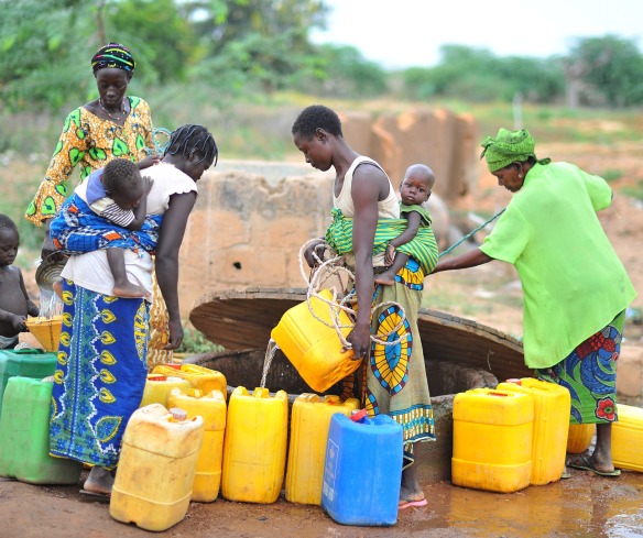 Women and children stand by a well, gathering water.